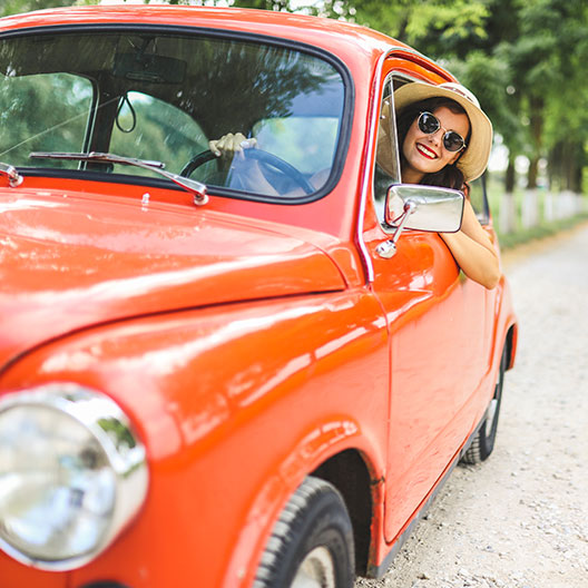 woman driving vintage red vehicle, sticking her head out of the window