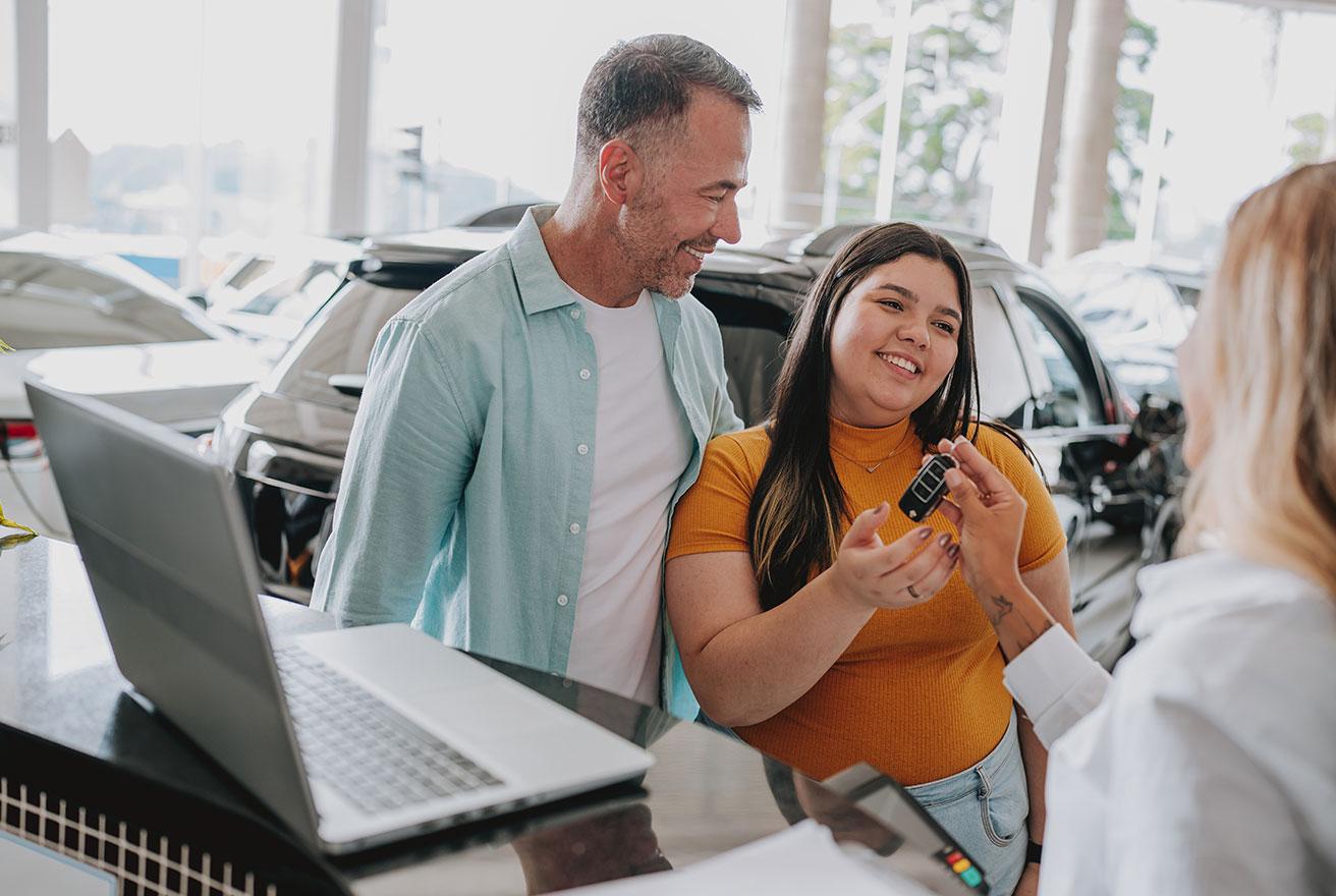 dad smiling at daughter while she gets keys at new car dealership