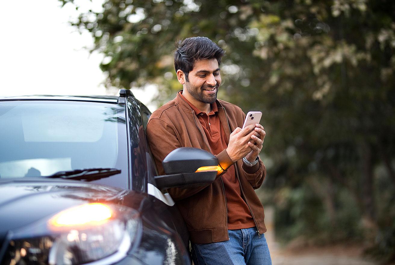 man leaning on car while smiling and using phone